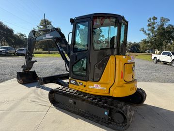 Compact yellow mini excavator parked on concrete under clear sky.