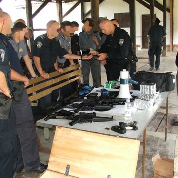 Police officers inspecting firearms and equipment on a table during a training session.