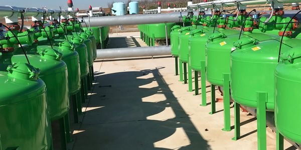 Rows of green industrial tanks connected by pipes in an outdoor facility.