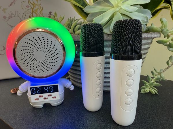 Two white microphones and a colorful speaker on a table with plants in the background.