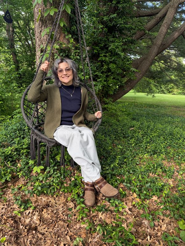 Person relaxing on a hanging chair outdoors surrounded by greenery.