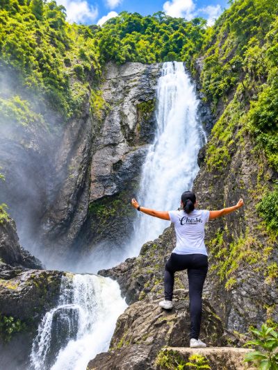 Person enjoying a waterfall in a lush green environment.