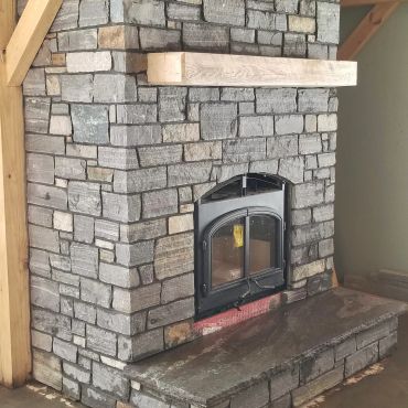 Stone fireplace with a glass door and wooden mantel.