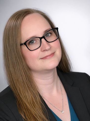 Professional woman with glasses and long hair smiling gently.