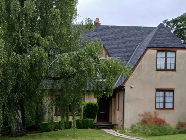 A cozy house with a steep roof and lush greenery in front.