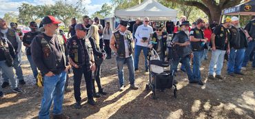 Group of bikers gathered outdoors near tents on a sunny day.