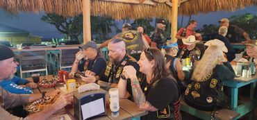 Group of bikers socializing under a thatched roof at night.