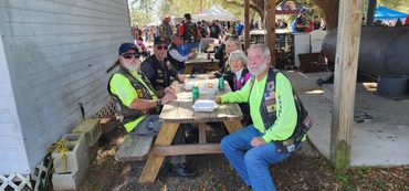 Veterans in neon shirts and biker vests enjoy a meal at an outdoor gathering.