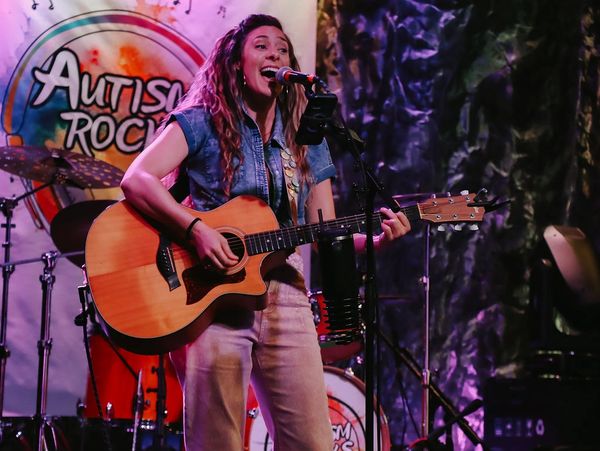 Female musician passionately singing and playing guitar at Autism Rocks event.
