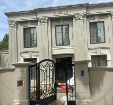 Elegant two-story house with ornate columns and black gate.