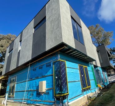 Modern two-story house under construction with blue tarp wrap.