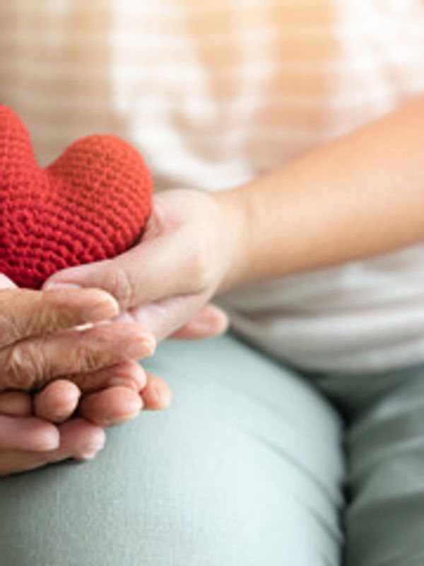 Two people holding a red knitted heart together.
