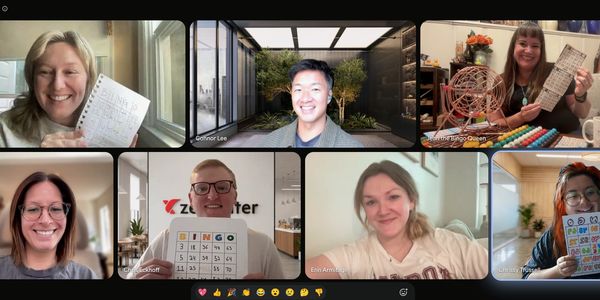 Group video call with smiling participants holding bingo cards and crafts.