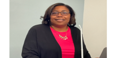 Lisa D. Dance, African American woman in pink shirt & black sweater, behind podium with microphone