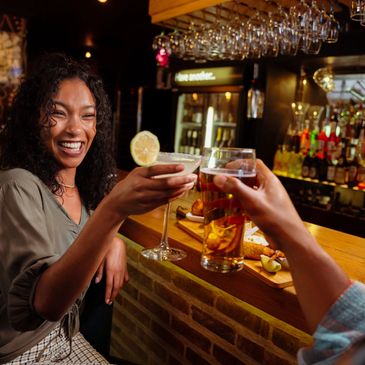 Two people clinking drinks and enjoying a lively bar atmosphere.