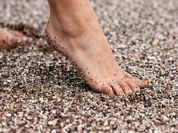 Barefoot stepping on small pebbles, grains sticking to skin.