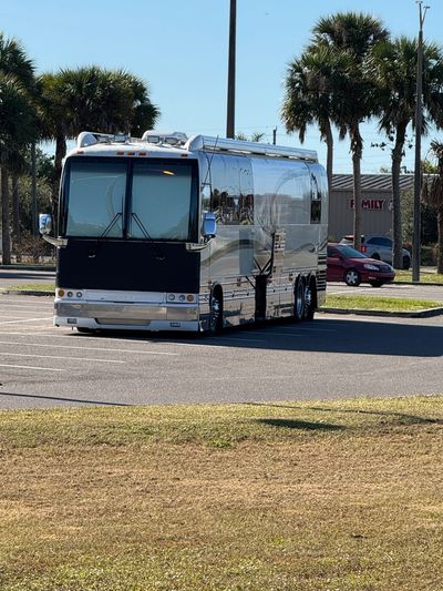 A shiny, modern motorhome parked in a sunny lot with palm trees in the background.