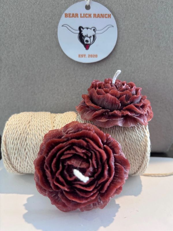 Two intricately carved flower-shaped candles in front of twine spools with a Bear Lick Ranch tag.