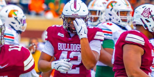 Football player in maroon Bulldogs jersey adjusting helmet during the game.