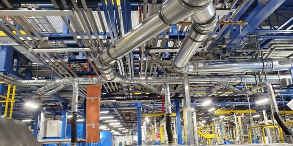 Complex network of metal pipes and industrial equipment in a factory setting.
