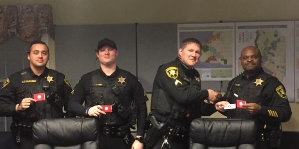 Four police officers posing with badges in an office setting.