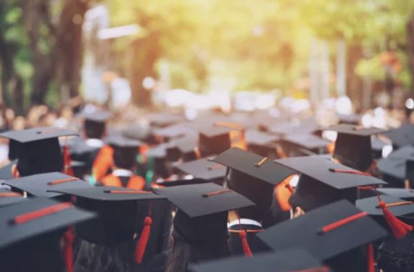 Crowd of graduates wearing black caps with red tassels outdoors.