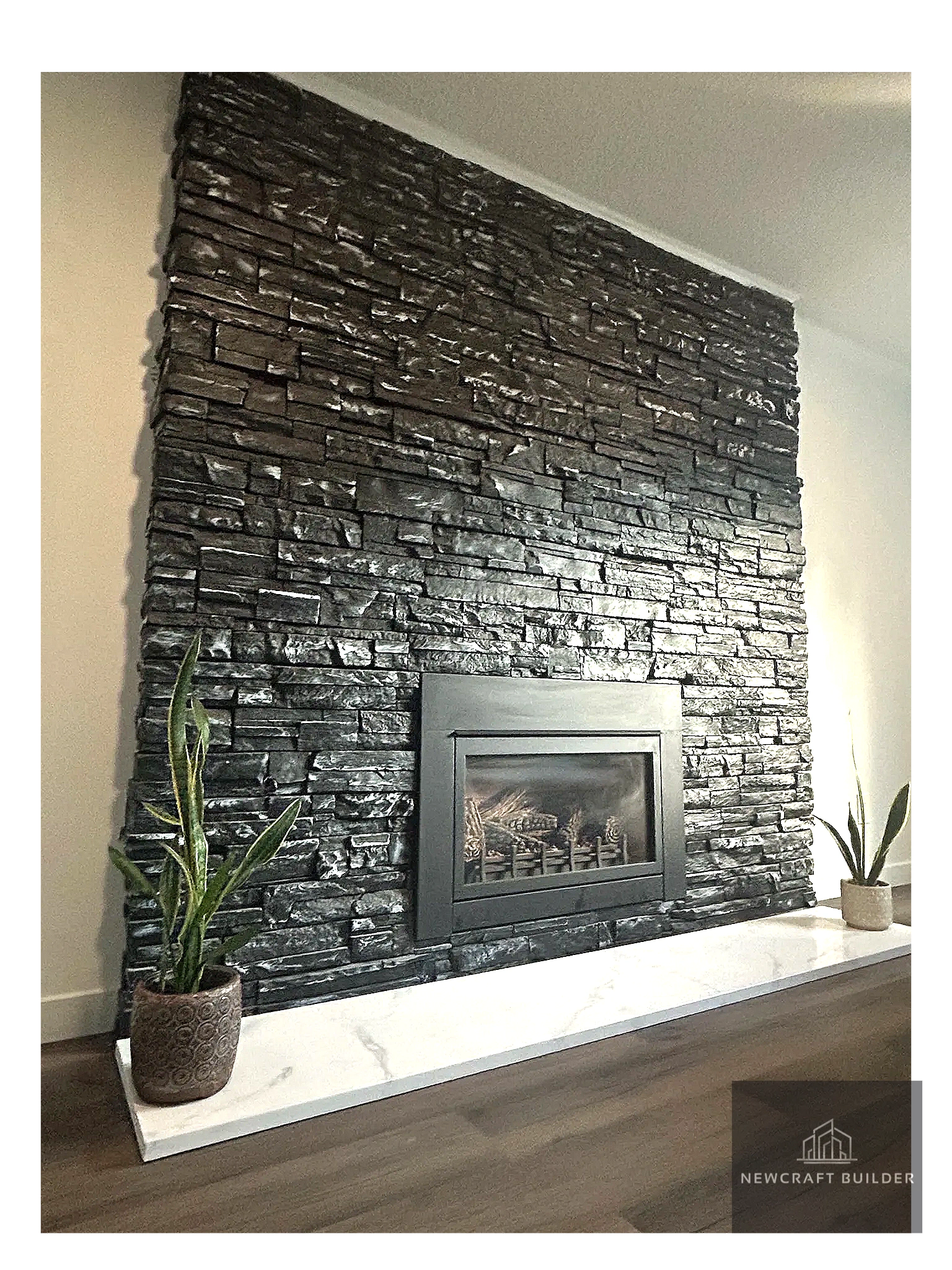 Modern black stone fireplace with two potted plants on a white marble hearth.