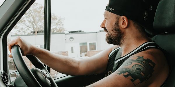 Bearded man with tattoo driving a vehicle, looking outside.
