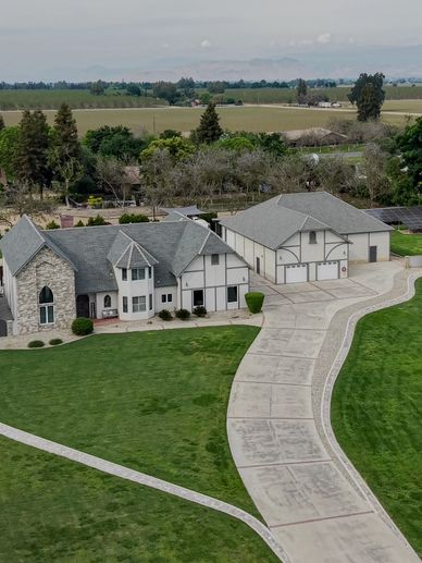 Large country house with a long driveway and green lawn.
