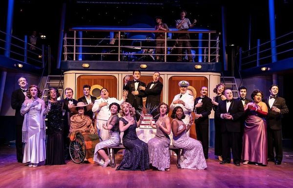 Cast of a theatrical production posing on stage in elegant costumes.
