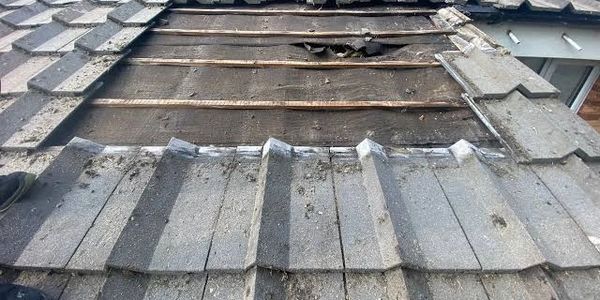 A section of roof tiles removed revealing damaged wooden beams underneath.