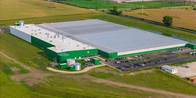 A large green and white industrial warehouse surrounded by fields.