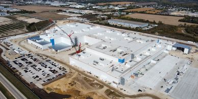 A large industrial building under construction with cranes and parking lots.