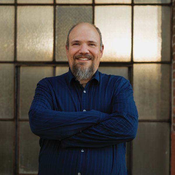 Smiling man with a beard in a blue shirt.