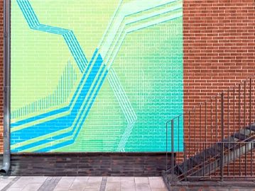 Colorful geometric mural on a brick wall next to metal stairs.