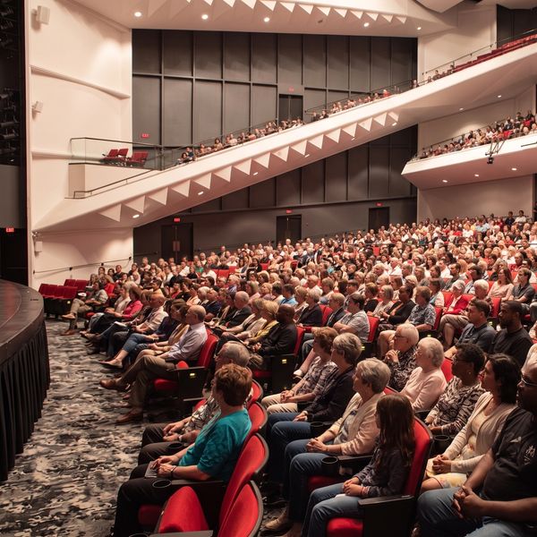 A large audience attentively watching a performance in a modern theater.