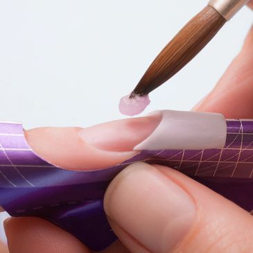 A nail technician is applying acrylic onto a customer's natural nail.