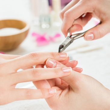 A nail technician is using a clipper to clean up a nail cuticle. 