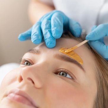 A nail technician applies wax onto a customer's forehead near the eyebrow for waxing. 