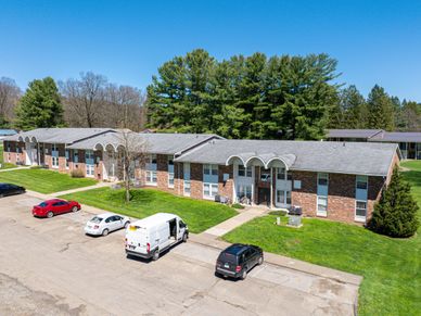 A two-story brick apartment building with parked cars in front on a sunny day.