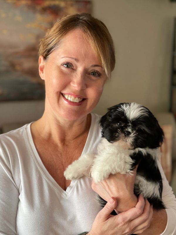 Smiling woman holding a fluffy black and white puppy indoors.