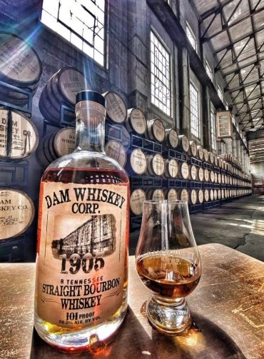 Bottle and glass of Tennessee straight bourbon whiskey in a barrel warehouse.