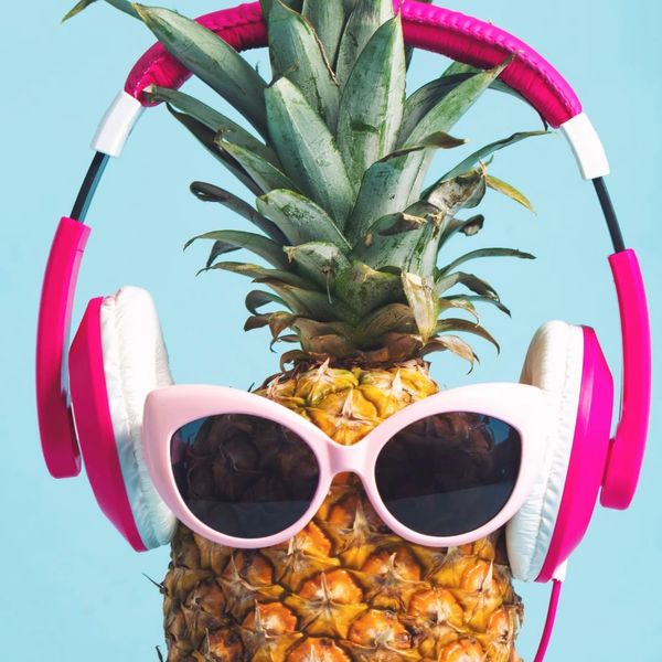Pineapple wearing pink sunglasses and headphones against a blue background.