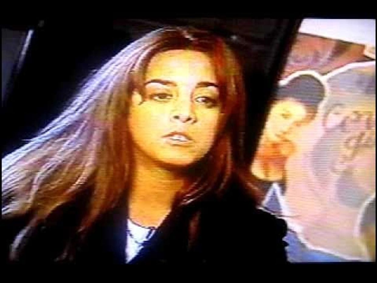 Young woman with long hair looking serious in a dimly lit room.