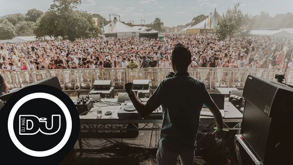 DJ performing live to a large outdoor crowd at a music festival.
