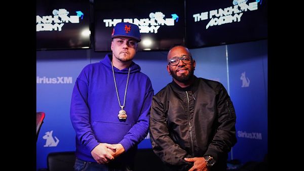 Two men posing in front of The Punchline Comedy screens at SiriusXM studio.