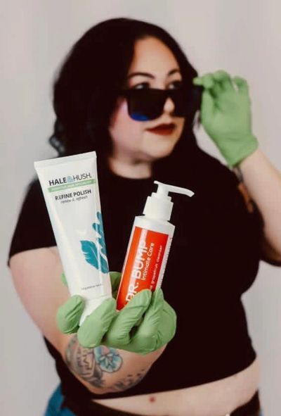 Person wearing green gloves and sunglasses holding two skincare products.