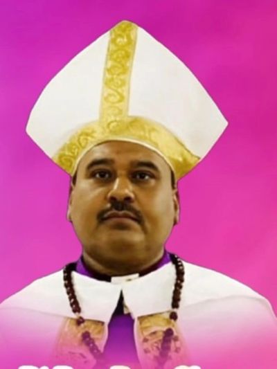 Man wearing a white and gold ceremonial religious hat against a purple background.