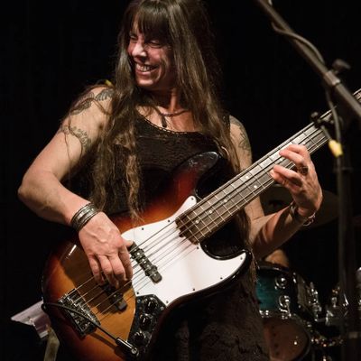 Woman passionately playing electric bass guitar on stage.