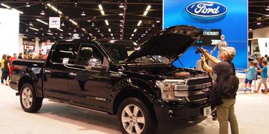 Man photographing a black Ford pickup truck at a car show.
